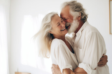 A beautiful elderly couple hugs and smiles in a bright room.