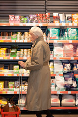 Senior adult female is shopping at a grocery store. She is reading nutrition facts on the label. She is shopping alone.