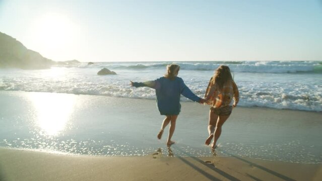 In a cinematic moment, two millennial friends sprint barefoot along a natural, untouched beach, their laughter echoing the essence of pure friendship. Freedom travel lifestyle of new generation