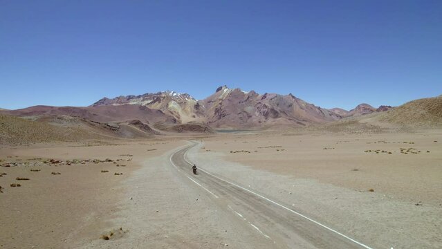 man on motorcycle followed by drone discovering a lonely desert road with mountains and lagoons