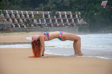 A beautiful girl does gymnastics on the beach. Girl with red hair. Sandy beach.