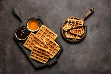 Homemade Belgian waffles with honey and liquid chocolate, dark rustic background. Top view, flat lay