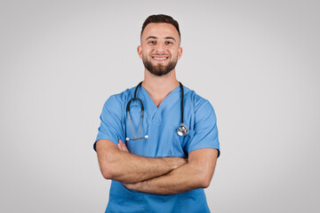 Confident doctor in blue scrubs posing with crossed arms and smiling