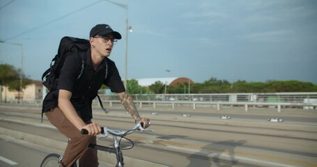 Young man with a backpack, cycles along the bike lane on commuting bike. Office worker or student hurry for a work or school. Cycling commuting and green lifestyle promoting. 