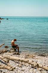 mężczyzna czytający ksiązkę naplaży w słońcu, Czarnogóra, Bigovica, Morze Adriatyckie,...
