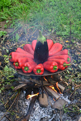 Round pile of red peppers and eggplant on the grill outside