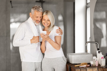 Happy senior couple checking smartphone together in bathroom during their morning routine