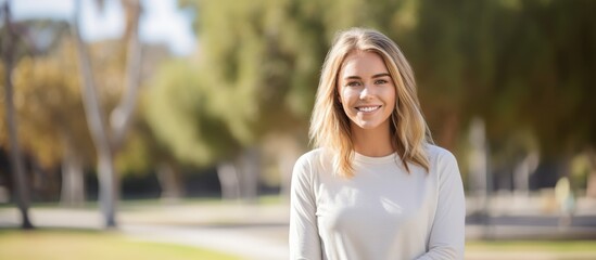 A park is where a young woman with blonde hair stands confidently wearing a smile on her face - Powered by Adobe
