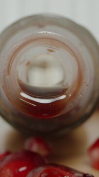 Vertical video. On a wooden table lies a bottle from which pomegranate juice is dripping. Pomegranate fruits and spilled juice. On a white background. Dolly slider extreme close-up.