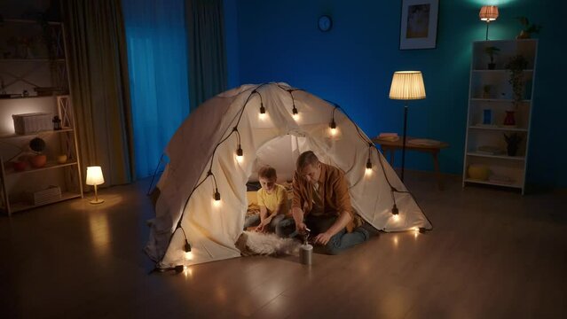 Dad and son in a tent in the living room. The man shows the little boy the principle of operation of a camping gas burner, lights it with matches, adjusts the fire. Video 2 in 1. Slow motion.
