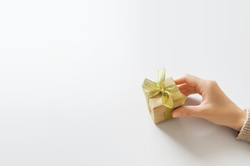 female hand holding a small gift box with a golden bow on a white table, mockup, space for text. Mother's Day, Valentine's Day, Christmas and New Year gifts concept