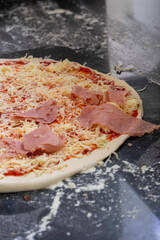 Delicious pizza topped with tomato sauce, cheese, ham, and pepperoni, ready to be baked. 