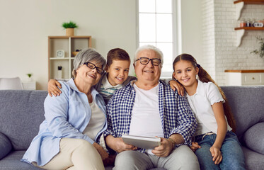 Portrait of a happy grandparents sitting on sofa with their grandchildren boy and girl at home with...