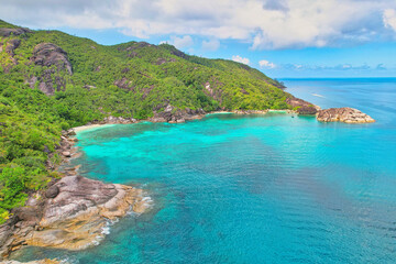 Fototapeta premium Drone shot of Anse du riz, rice beach beach, transparent sea, lush forest and granite stones, docked and passing boat, Mahe, Seychelles 1