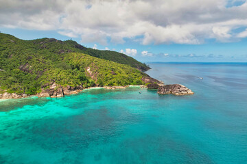 Drone shot of Anse du riz, rice beach beach, transparent sea, lush forest and granite stones, docked and passing boat, Mahe, Seychelles 2