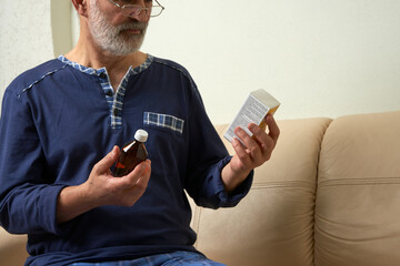 An older man wearing glasses reads the instructions on the packaging of a medicine.