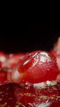 Vertical video. On a black background, Red Pomegranate Seeds with juice dripping from above, slowly cascading over the seeds. Close-up.