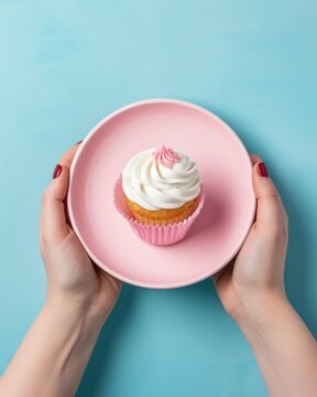 A single cupcake is gently held on a small plate by the woman's hands.