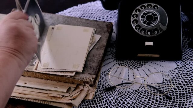 middle-aged female hands hold old photos 50s, 60s, retro phone, photo albums, handmade lacy on table, concept of genealogy, memory of ancestors, family tree, childhood memories