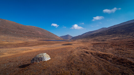 A quiet landscape, a strong vanishing point, a big white rock in a dry landscape under a blue sky