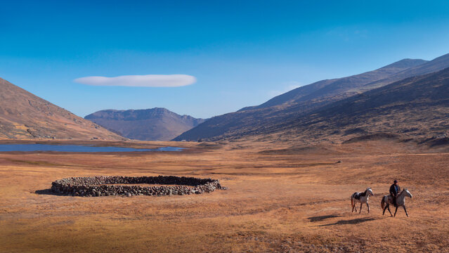 A Peruvian farmer riding a white horse through a minimalist Andean pampa in autumn time