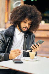 a young man having breakfast in a cafeteria while using a mobile phone