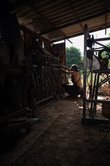 Wide angle view of a blacksmith checking the measurements of a grating in his workshop.