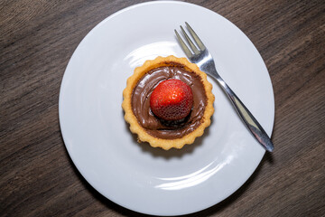 Small cake with a strawberry and chocolate cream on a plate