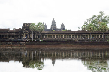 Fototapeta na wymiar Ancient Buddhist Temple Ruins of Angkor Wat in Siem Reap, Cambodia. Reflection of the temples in the lake's water on a cloudy day.