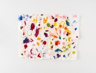 Crumpled paper splattered with vibrant multicolor paint on white background. Minimal composition. Flat lay.