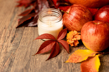 Burning candle on the table next to apples and grape leaves. Autumn Composition