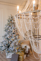 Large crystal chandelier.Christmas interior in white colors. Furniture in the living room. eleganttree with garlands.