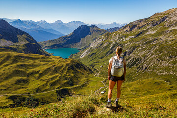 eine junge Frau steht an einem Wanderweg auf einem Berg und schaut auf den Spullersee in Vorarlberg...