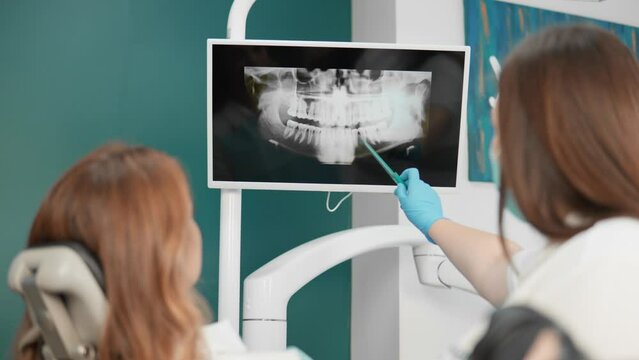 The dentist shows the woman X-rays of her teeth for a detailed examination. The dentist uses panoramic tomography to accurately diagnose problems in the oral cavity.