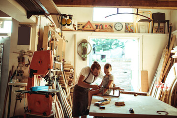 Father guiding his daughter in crafting wood in their workshop