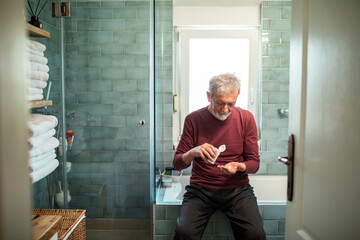 Senior man taking his medication in the bathroom at home - obrazy, fototapety, plakaty