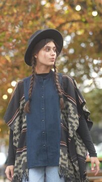 In the streets of the autumn city, a fashionable girl in a hat and hippie outfit passes by.