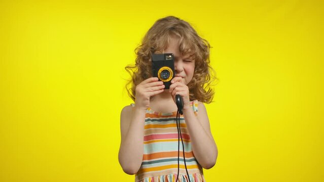 Litttle curly girlp hotographer is using retro camera for shooting photo