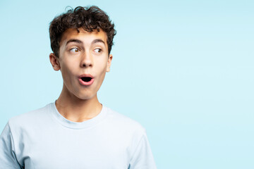 Portrait of excited positive teenage boy looking away isolated on blue background