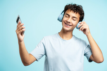 Portrait of smiling teenage boy wearing headphones listening to music, holding mobile phone - obrazy, fototapety, plakaty
