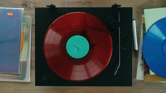 Male hand turns on classic gramophone and disco sound music fills the room or studio. Top view of vinyl record player surrounded by colorful vinyl discs. 