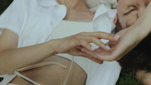 Close-up lovers lie on the lawn and gently touch their fingers. Close-up shot of female hand lies on top of the man's hand, gentle touches with the hands. Close-up holding hands., slow motion.