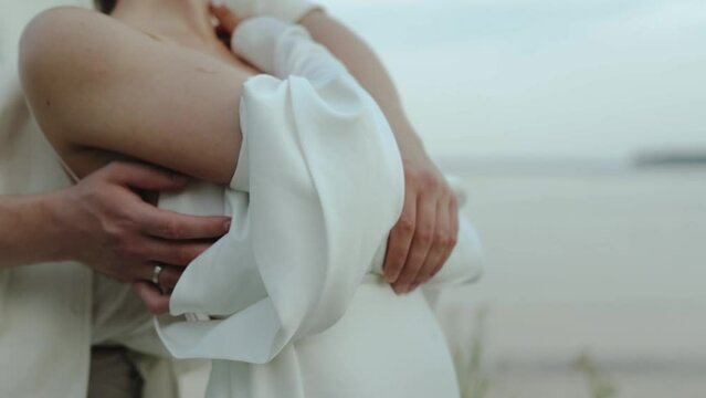 Close-up romantic couple in love standing on the beach, man hugging woman from behind. Bride ang groom holding hands, Cuddling, flirting outdoors.