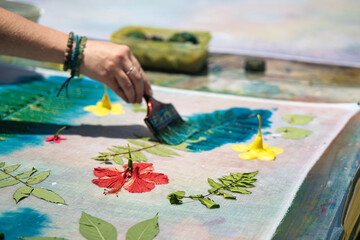 White skin woman, painting over leaves with cloth printing ink at workshop for her pareo making,...