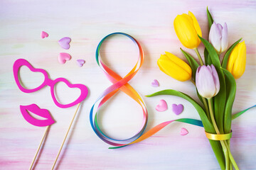 Beautiful background postcard for Women’s Day on March 8 with a bouquet of tulips, a figure-eight ribbon, hearts and decorative glasses and lips.