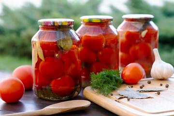 three cans of canned tomatoes stand on a table in the garden, spices, garlic and tomatoes lie nearby