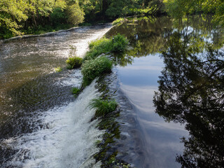 Vista de una cascada de agua transparente rodeado de naturaleza verde y límpia reflejando el paisaje del pueblo de Allaritz en el río, en Galicia visitando España en verano de 2021