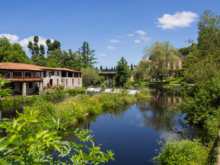 Fototapeta na wymiar Paisaje natural del pueblo de Allaritz en Orense, con un molino plantas verdes y árboles alrededor de un río con las nubes y cielo azul reflejados, en verano de 2021, viajando por Galicia, España.