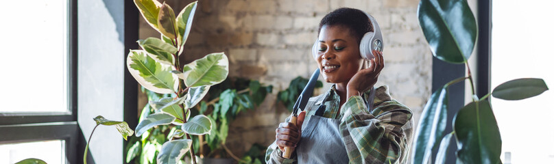 Concept of simple life pleasures, work life balance, mental health, relaxation at home. Attractive young African American woman doing home gardening, repotting plants, taking care about flowers banner