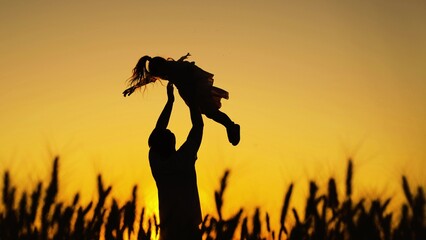 Dad plays with his daughter, throws child up into sky with his hands, happy child. Childish, superhero, fly. Family game concept. Father, child, little girl having fun together in park against of sun